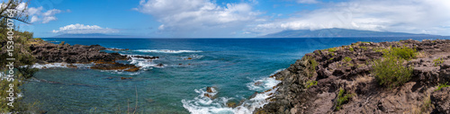 Panoramic view of a rocky coastline with blue ocean and sky.