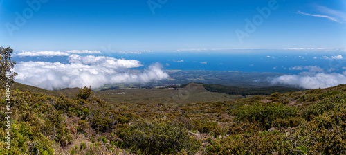 Panoramic view from a mountain top, with clouds, ocean, and vegetation.