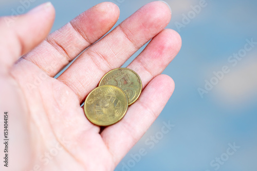 A person is expertly holding two shiny coins in the palm of their hand