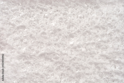 A high-angle, close-up shot captures the texture of a white foam material, showing numerous small, clear bubbles forming its surface
