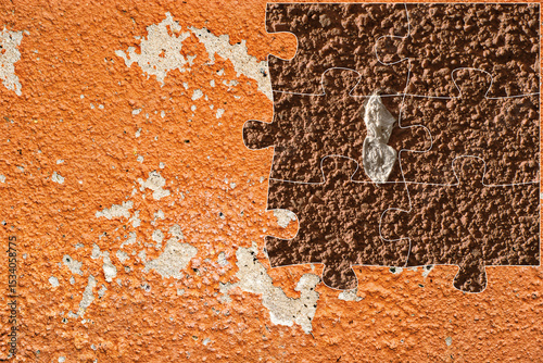 Pieza de rompecabezas sobre una pared naranja de textura rugosa con mancha natural, que muestra contraste entre superficies, deterioro e imperfección.