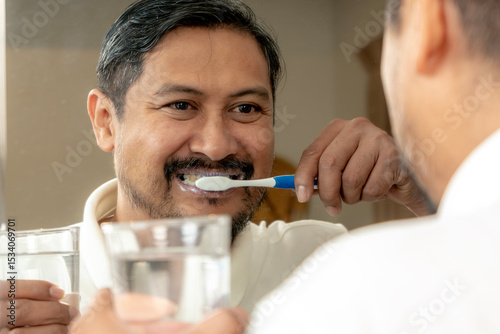 Morning routine of a young man brushing his teeth in front of the mirror in a home bathroom.