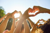 Group of people making heart shape gesture standing in summer park at sunset. Thankful young friends doing love sign raising hands up in nature against blue sky. Friendship, care and people concept