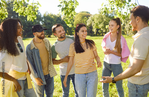 Photos Outdoor shot of cheerful friends meeting together in park, discussing something, standing in circle, having smiles on faces, enjoying free time, good summer weather