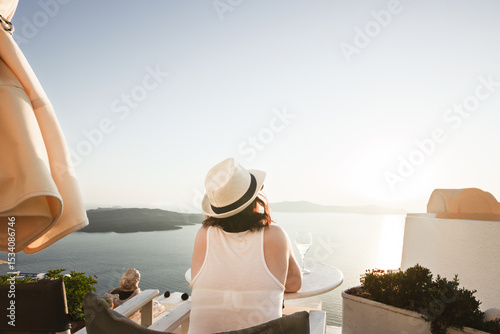 A woman enjoys a scenic sunset view over the Aegean Sea from a Santorini terrace with a glass of wine.