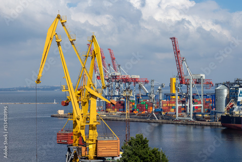 A wide shot shows the busy Port of Odesa Ukraine featuring towering gantry cranes moving numerous brightly colored shipping containers, with the city visible in the background, maritime industry