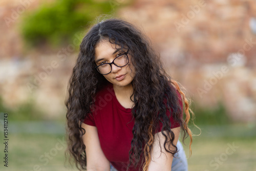 teenaged girl with glasses leaning forward with long dark curly hair falling over her shoulders