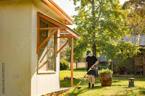 Teenage boy using line trimmer on lawn edging in country garden