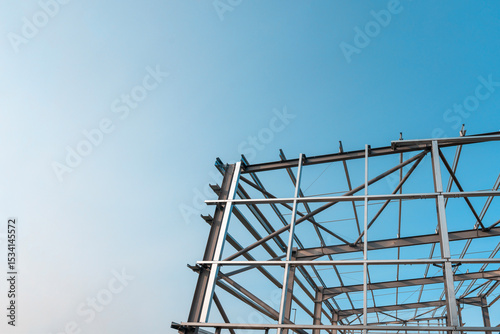 Steel framework of a modern building rising against a clear blue sky during daytime construction activity