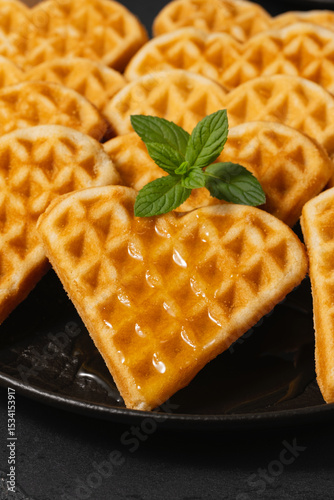 Delicious heart-shaped waffles with syrup and mint on a black plate, perfect for breakfast or dessert