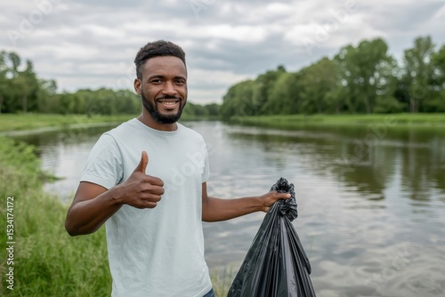 Smiling volunteer man with garbage bag near river and trees
