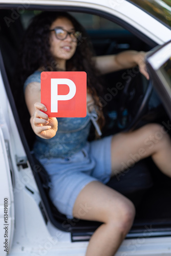 teenager sitting in driver's seat of car holding red P plate