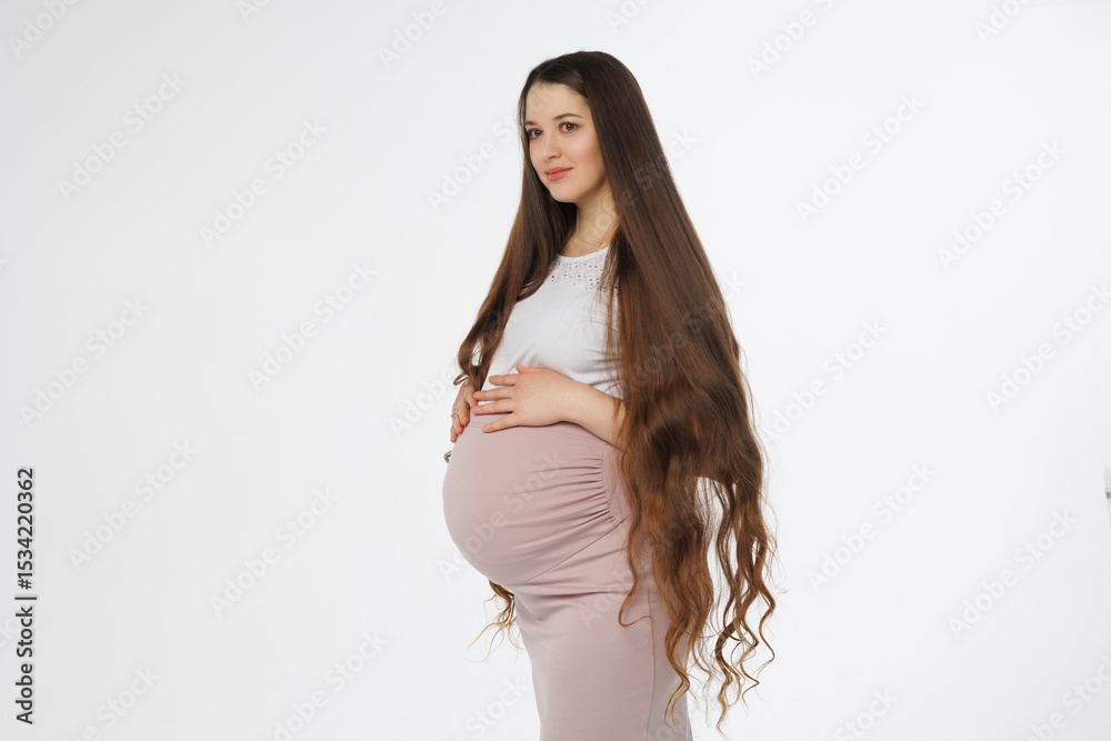 Fototapeta premium Pregnant woman in dress with very long hair on white background. Dreamy tender girl expecting a child. Portrait of beautiful pregnant woman in white shirt, smile. Window