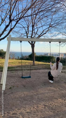 Young woman swinging on a hillside swing at sunset with sea view, slow motion
