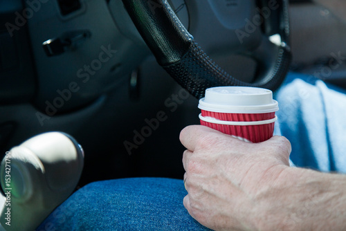 Man holding a coffee in a takeaway cup while driving