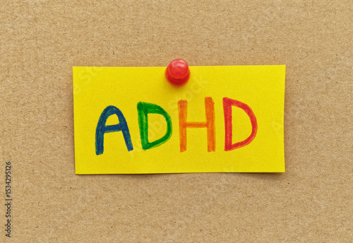 A yellow paper note with the abbreviation ADHD on it pinned to cardboard. ADHD is Attention deficit hyperactivity disorder.