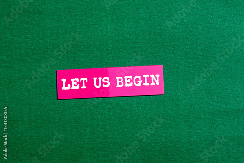 Let us begin message written on pink paper sticker on green background. Conceptual let us begin symbol. Copy space.