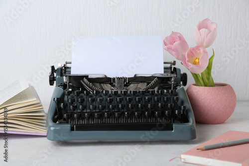 Vintage typewriter with paper sheet, tulips and book on grunge table near white wall
