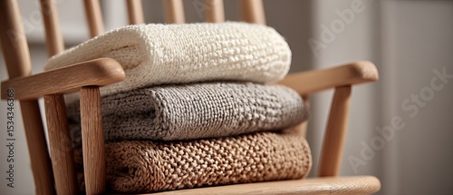 Soft knitted baby blankets folded on a rocking chair, neutral tones, cozy baby room atmosphere