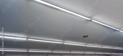 A series of LED tube lights installed on a ceiling. A row of lights are hanging from the ceiling in a room. The lights are white and are evenly spaced.