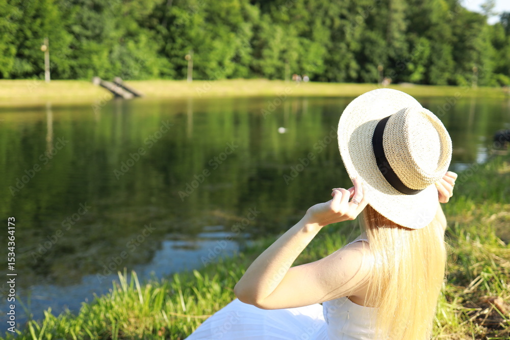 Fototapeta premium Woman in a white dress enjoying a sunny day by a serene lake surrounded by lush greenery