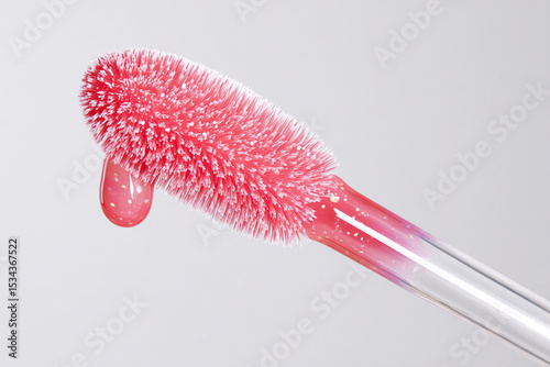 A bright pink cosmetic applicator features soft bristles, holding a glossy liquid droplet at its tip