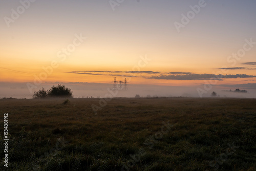 Morning fog shrouds high-voltage power transmission towers in rural area