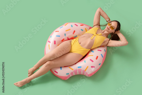 Female tourist with swim ring lying on green background, top view