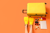 Female legs in flippers with travel accessories on orange background, top view