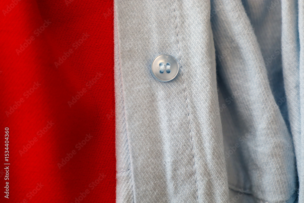 Blue shirt fabric with a single button in close-up, contrasting with a bright red background. This combination of colors and textures creates an interesting visual effect, highlighting clothing detail Blue shirt fabric with a single button in close-up, contrasting with a bright red background. This combination of colors and textures creates an interesting visual effect, highlighting clothing detail