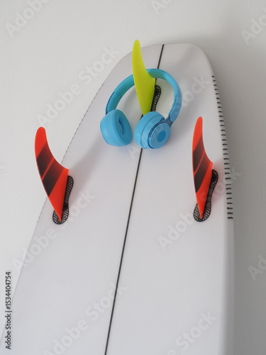Surfboard with vibrant red and green fins. Blue headphones rest on top, combining surf culture with music.