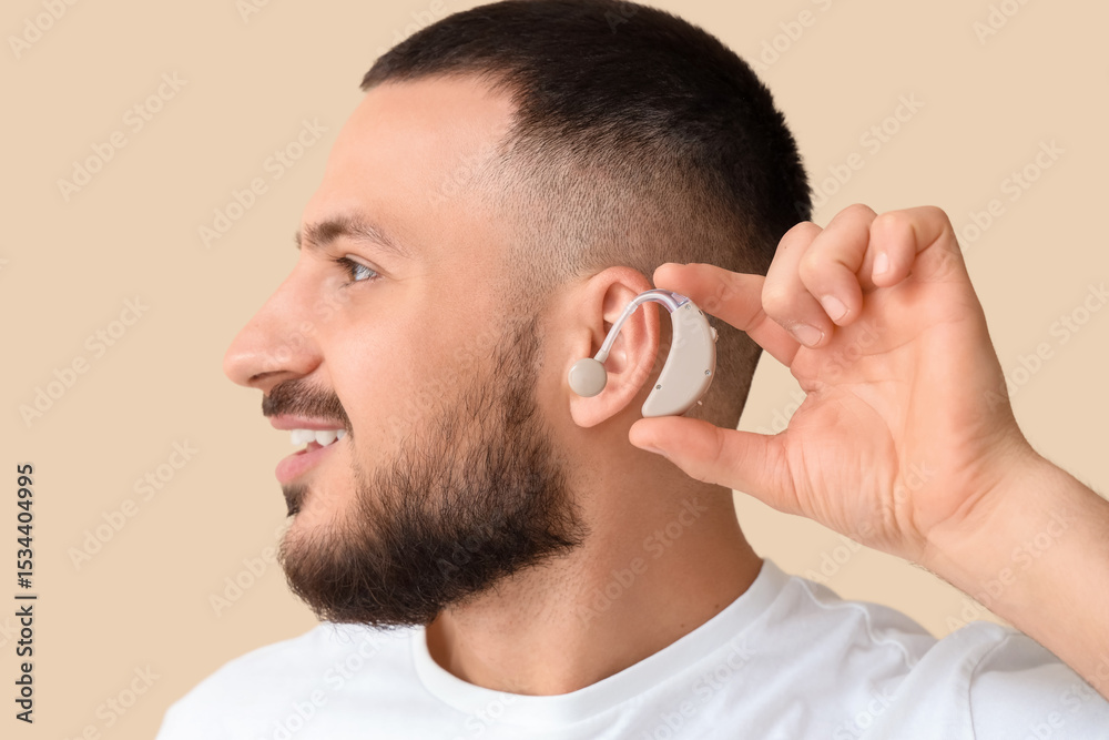 Fototapeta premium Young man with hearing aid on beige background, closeup