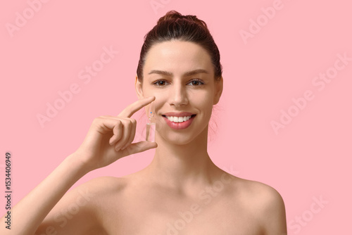 Smiling young woman with ampoule on pink background