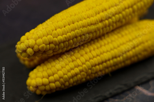 Close-up of yellow, ripe, peeled ears of corn with large grains lying sideways against a dark background in the center. The concept of healthy nutrition, natural iron, corn cultivation. High quality photo