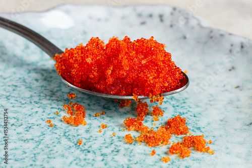 a spoon with orange flying fish caviar, Tobiko, on a light blue plate, caviar for rolls and sushi, close-up,