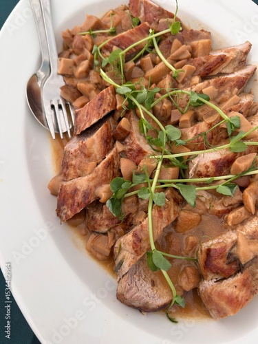 Sliced veal in creamy mushroom sauce topped with fresh microgreens on a white plate