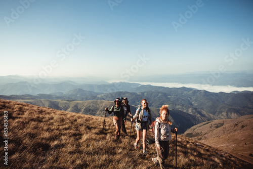 Young and diverse group of female friends hiking in the mountains and looking at the sun setting behind a nearby hill