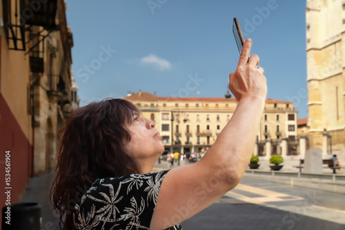 Tourist filming leon cathedral in plaza de regla, leon, spain, using a smartphone