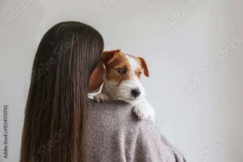 Back view of a brunette woman holding a dog. Copy space background.
