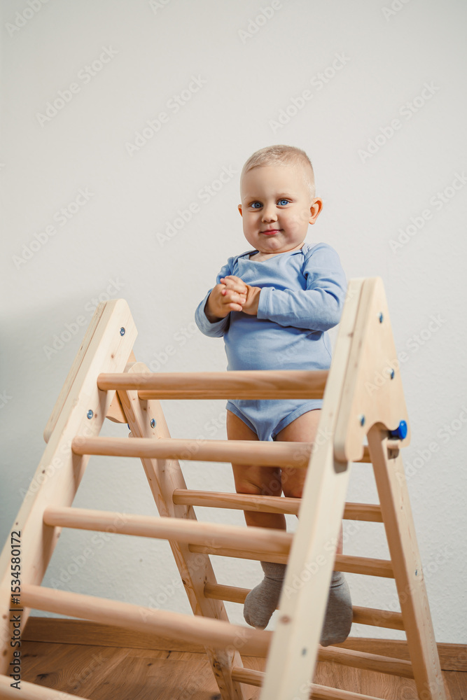 An absolutely adorable baby is happily standing upright on a colorful wooden climbing frame situated in a modern playroom, showcasing the carefree spirit and joy of early childhood and playtime An absolutely adorable baby is happily standing upright on a colorful wooden climbing frame situated in a modern playroom, showcasing the carefree spirit and joy of early childhood and playtime