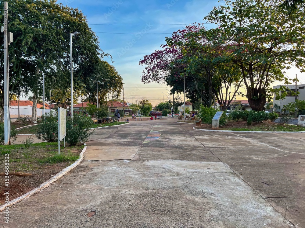 Obraz premium View of a concrete park pathway with trees and benches under a blue and yellow sky at sunset time