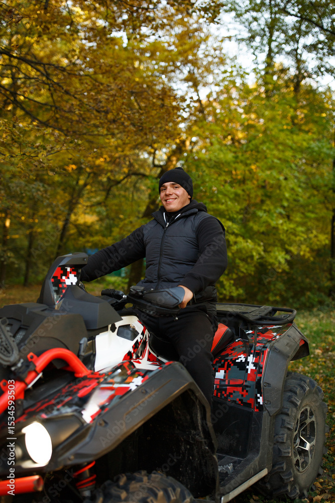 Obraz premium Man riding an ATV in autumn forest enjoying an off-road adventure. Concept of outdoor activity, freedom, thrill, and nature connection.