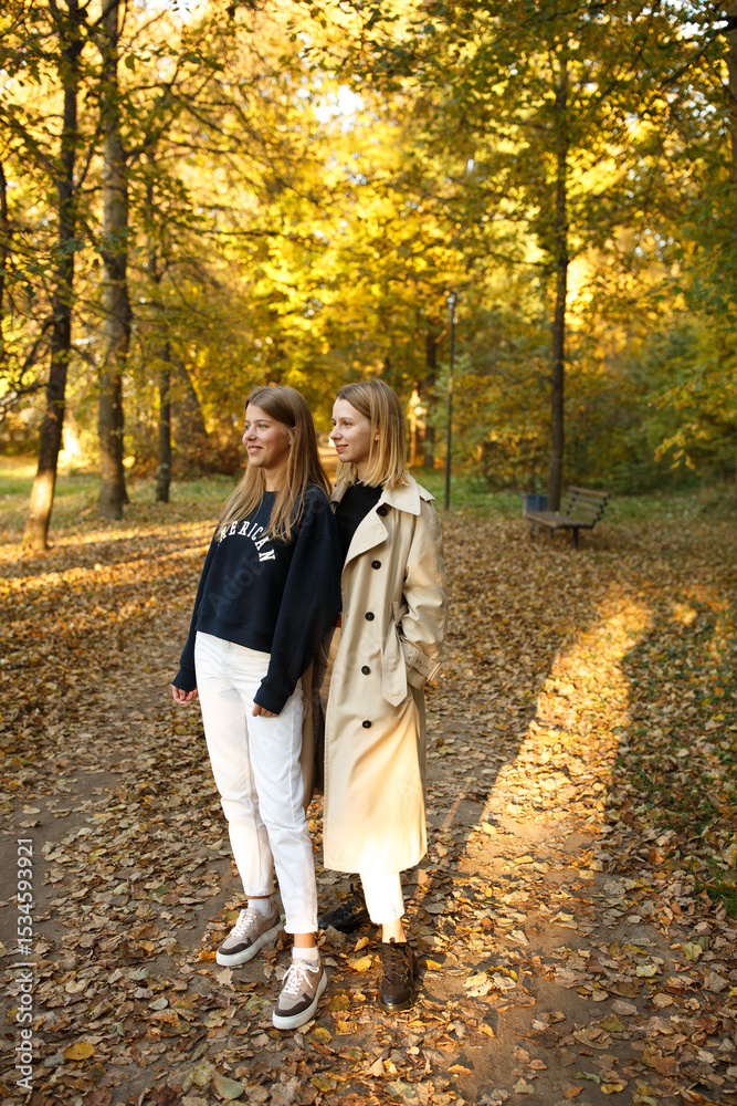 Fototapeta premium Two friends pose together in a golden autumn park, enjoying the warm light and cozy atmosphere of a beautiful day.