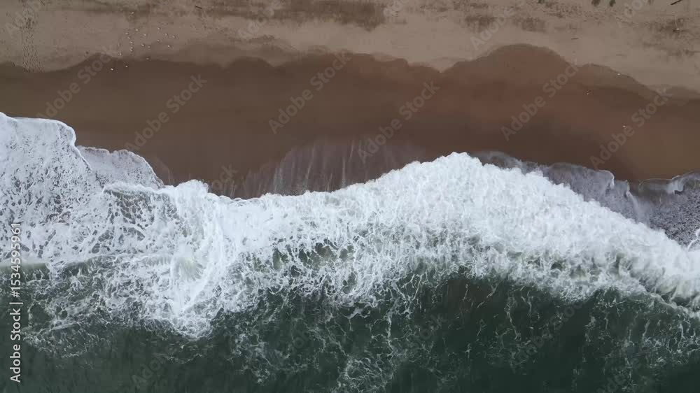 Toma aérea descendente que se acerca suavemente al mar azul mientras las olas rompen con espuma en la costa catalana.