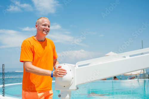Photography Man handling a pool chair lift, lifting and lowering from and into the water to provide access to the swimming pool for people with a physical disability