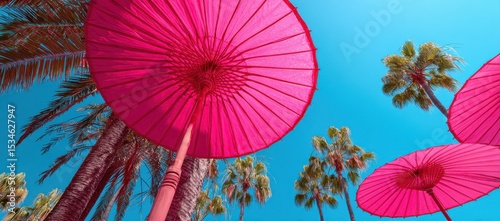 Pink beach umbrella and palm trees against clear blue sky, tropical vacation scene
