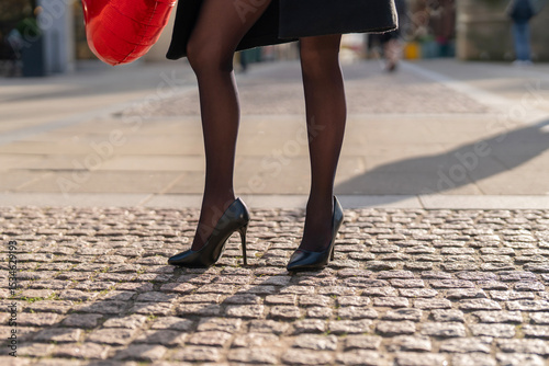 Elegant footwear shines on cobblestone pavement during a sunny urban stroll at midday with a vibrant red handbag adding a pop of color