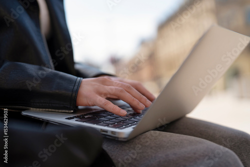 Person working on laptop outside in urban setting during daylight, focused on task while enjoying fresh air photo