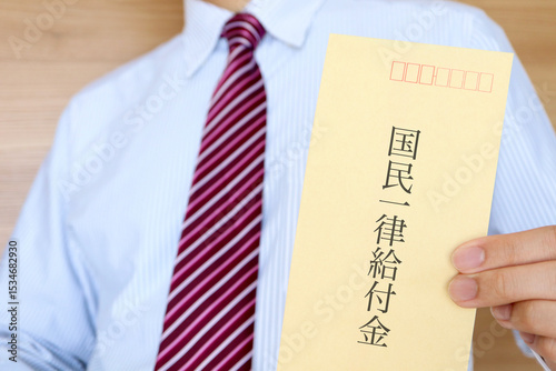 スーツの男性が国民一律給付と書かれた封筒を持っている