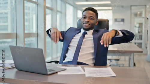 Confident businessman relaxing in modern office, with papers and laptop on desk, city view outside